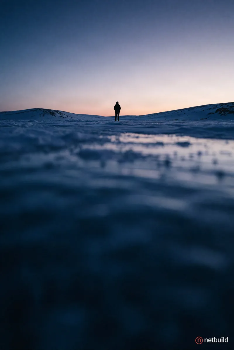 Cinematic extreme wide shot from a low angle perspective, featuring a solitary distant figure as a dark silhouette centered on a vast frozen expanse....